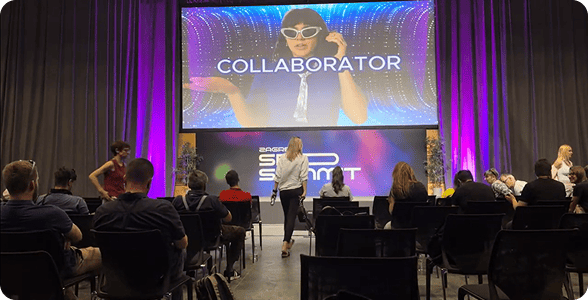 Miembros en una conferencia en Zagreb, sentados en sillas y mirando una gran pantalla que muestra el video promocional de Collaborator.